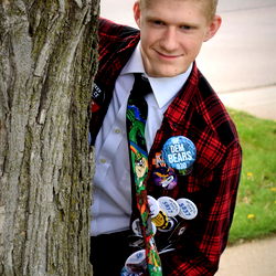 A young adult dressed as an enthusiastic fan of the Avengers, standing in front of a tree with badges attached to it.