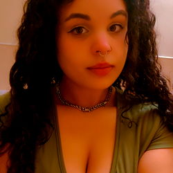 A woman with long curly hair, wearing a casual green shirt, posing for the camera in an indoor setting.