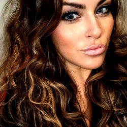 Shanda, a beauty with long hair and blue eyes, sharing her natural makeup look in casual attire. Her wavy hair is a stunning highlight of the image.