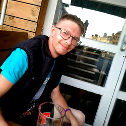 A man with glasses and a vest, sitting at an outdoor bar