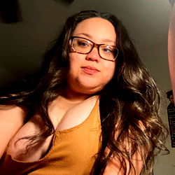 Luna Lovisa, a busty West Coast beauty with long hair and glasses, showcasing her cleavage in a low-cut top.