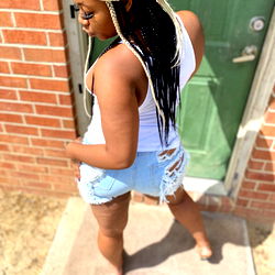 Shan Lashaee in a white tank top and jean shorts, standing on a sidewalk and looking back over her shoulder.
