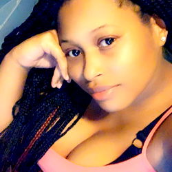 A young woman with long hair and tattoos, seated on a couch. OnlyFans model name is Shunti89