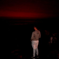 A solitary figure at the ocean under a pink sky at night