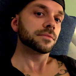 Luke, a young adult male with tattoos and a beard, is in a relaxed pose on a couch.