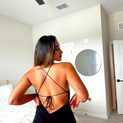 Amarys, a Florida OnlyFans model, showcasing an elegant black dress with a halter top and a low back detail, paired with her hair pulled back, in a tastefully decorated room.