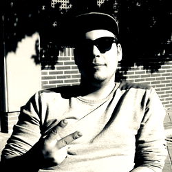 Casually Dressed Man Sitting Outdoors, Making a Peace Sign with One Hand