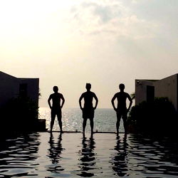 Three men in a poolside setting, with one on the left standing tall and two on the right leaning over him.