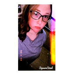 A young woman with glasses posing for a selfie in a kitchen or bathroom,
