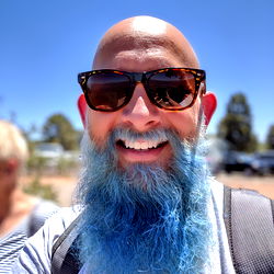 BluebeardSC, a bearded man with blue hair, posing for a picture in the sun.