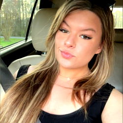 A young woman sitting in the driver's seat of a car, taking a selfie