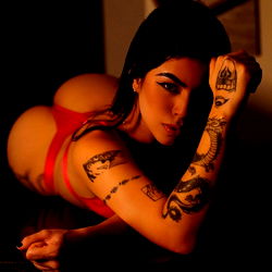 Bold and alluring model Zelda, from onlyfans, leans on surface with tattooed arms