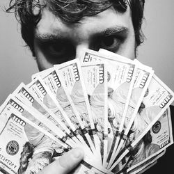 A stack of 100 dollar bills being held up by a man on OnlyFans