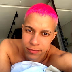 A young male model in a casual setting with pink hair and a colorful outfit.  