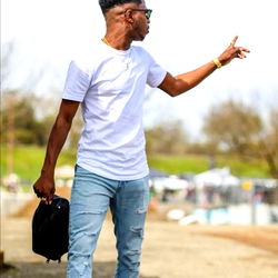 Harry, a young Colombian man in a casual outfit, possibly indicating an active lifestyle. He is walking on a dirt path with his hand extended towards the camera. His attire suggests that he might be heading out or coming back from a workout session.