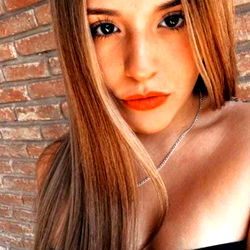 Model with long hair and neutral expression, posing against brick wall