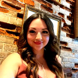 Darling621, the Ohio model captures her unique style in a vibrant photoshoot at an urban bar. Her outfit, composed of a purple top and complementary accessories, stands out against the rustic brick wall backdrop.